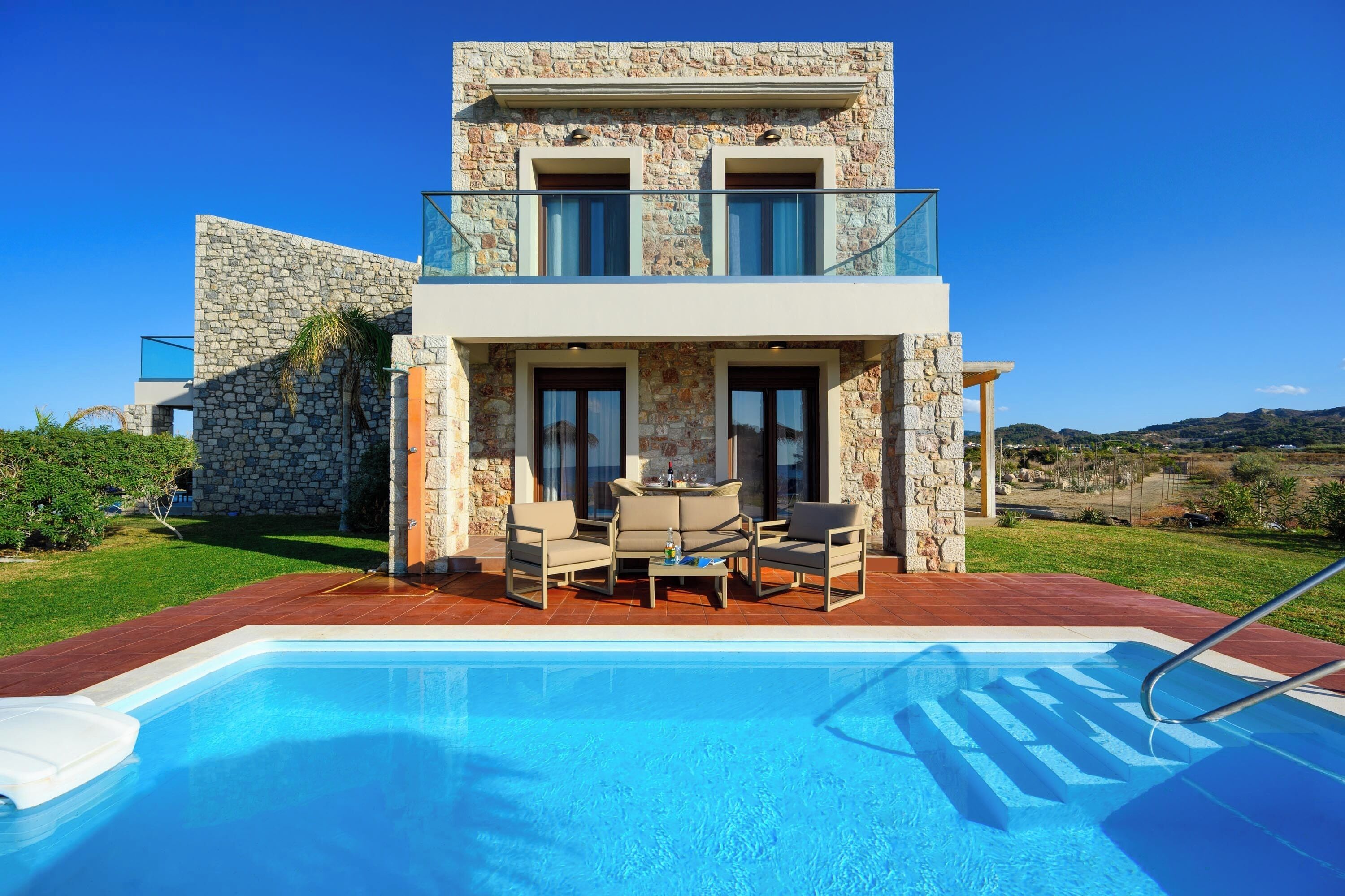 A modern two-story house with a swimming pool, outdoor furniture, and a stone facade.