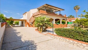 Ein zweigeschossiges Haus mit überdachter Terrasse, einem Kiesweg und umgebender Bepflanzung.