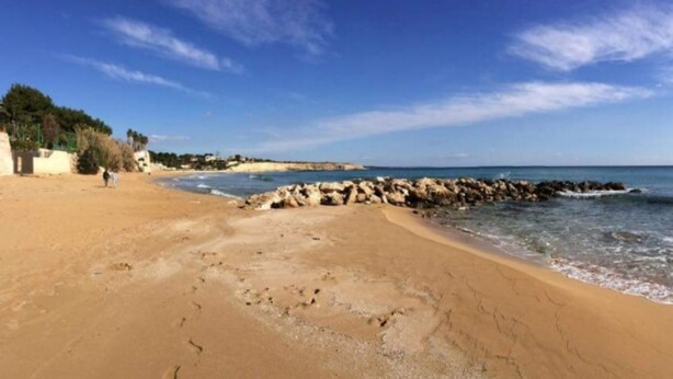 Ein sandiger Strand mit Felsen und blauem, klarem Himmel.