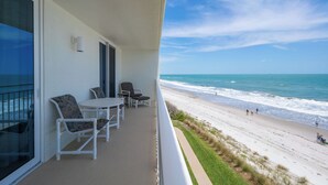 Ein Balkon mit weißer Möbel, einer Glastür und Blick auf den Strand.