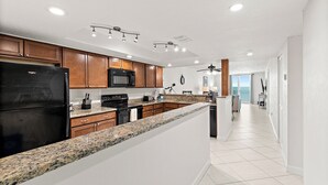 Eine moderne Küche mit Granit Arbeitsplatten, Holzschränken, einem schwarzen Kühlschrank, einer Mikrowelle und einem Deckenventilator.
