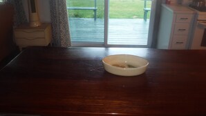 A wooden table with a bowl in the center, a window with a view of a patio, and a kitchen area with cabinets and appliances. - WATERSEDGE  GREAT VIEWS (Jefferson)