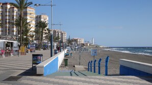 A coastal promenade with a beach, palm trees, and a lighthouse in the background. - Stylish apartment with sea views (Torrox)