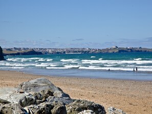 A coastal beach with rocky foreground, waves, and a distant town. - A stylish apartment set in an idyllic location in Watergate Bay. (Watergate Bay)