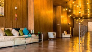 Eine moderne Hotellobby mit Holzboden, einer Couch mit bunten Kissen, einem Glastisch und einem weißen Sessel.