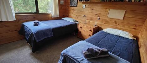 A cabin with two single beds, a wooden bookshelf, and a window with curtains.
