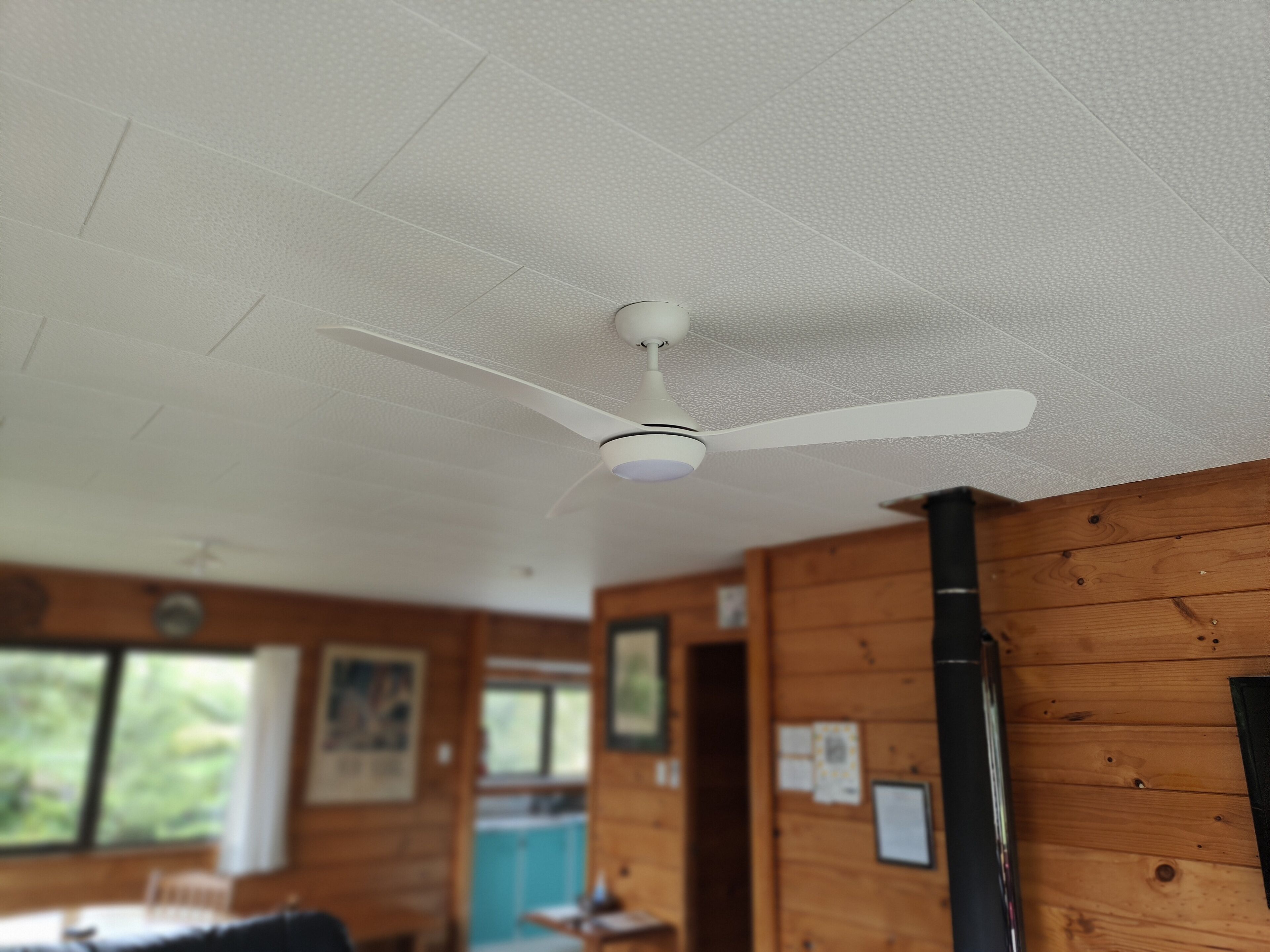 A ceiling fan in a room with wooden walls and a window.