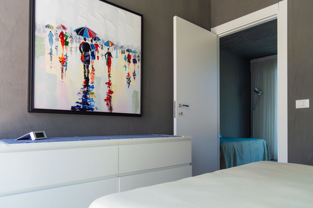 Un dormitorio con un cuadro abstracto grande, una mesita de noche blanca y una cama con cabecera azul.