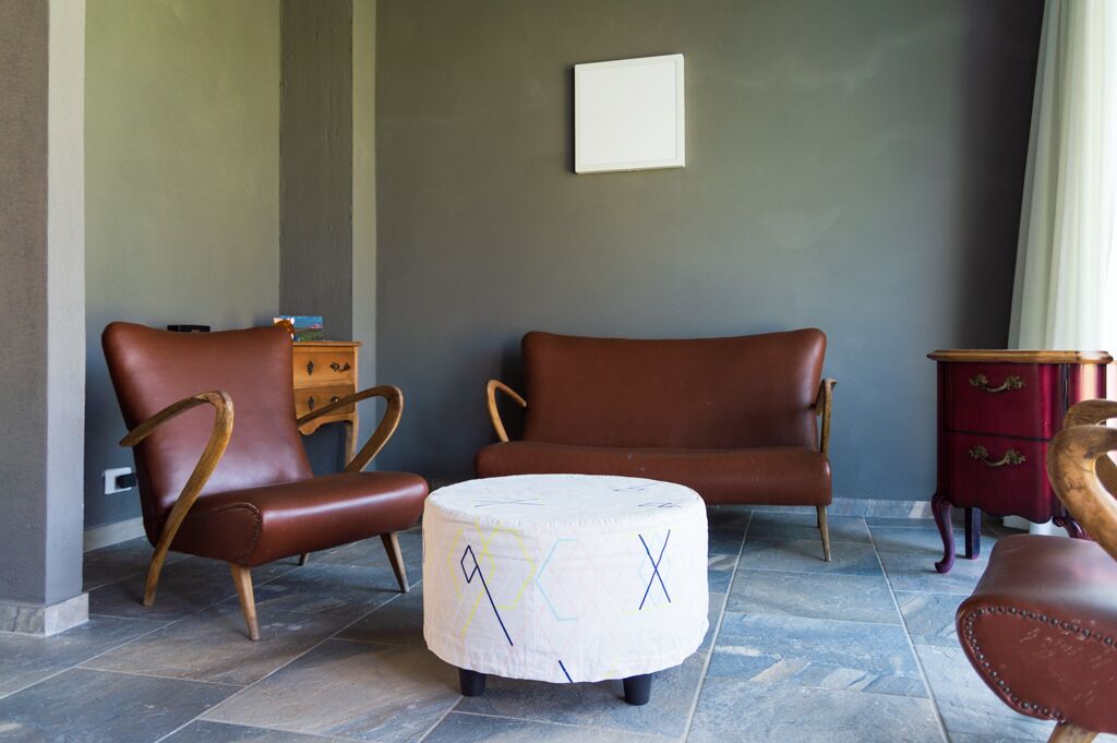 Une pièce comprenant deux fauteuils en cuir, une petite table d’appoint en bois et un pouf rond orné de motifs géométriques.