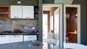 A modern kitchen with white cabinets, a marble countertop, and a dining area with a glass table. - Refined and welcoming Villa with private pool surrounded by nature (Omignano Scalo)