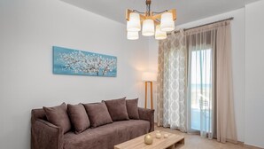 Een woonkamer met een bruine bank, een houten salontafel, een schilderij van een boom, een vloerlamp en een raam met gordijnen.