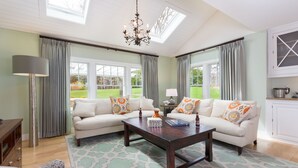A spacious living room with a large window, a chandelier, and a cozy seating area. - Cape Cod Intellectual Property (Eastham)