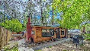 A wooden cabin with a chimney, a patio with outdoor seating, and a car parked nearby.