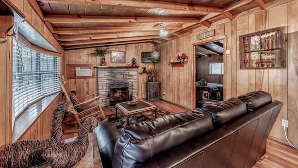 A wooden interior with a fireplace, leather sofa, and a television.