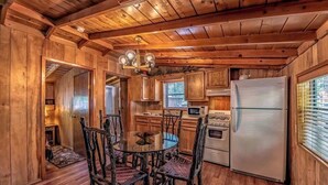 A wooden cabin interior with a dining table, chairs, a refrigerator, a microwave, and a stove.