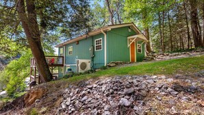 Ein grünes Haus mit einer Holzdiele, umgeben von Bäumen und einer felsigen Landschaft.