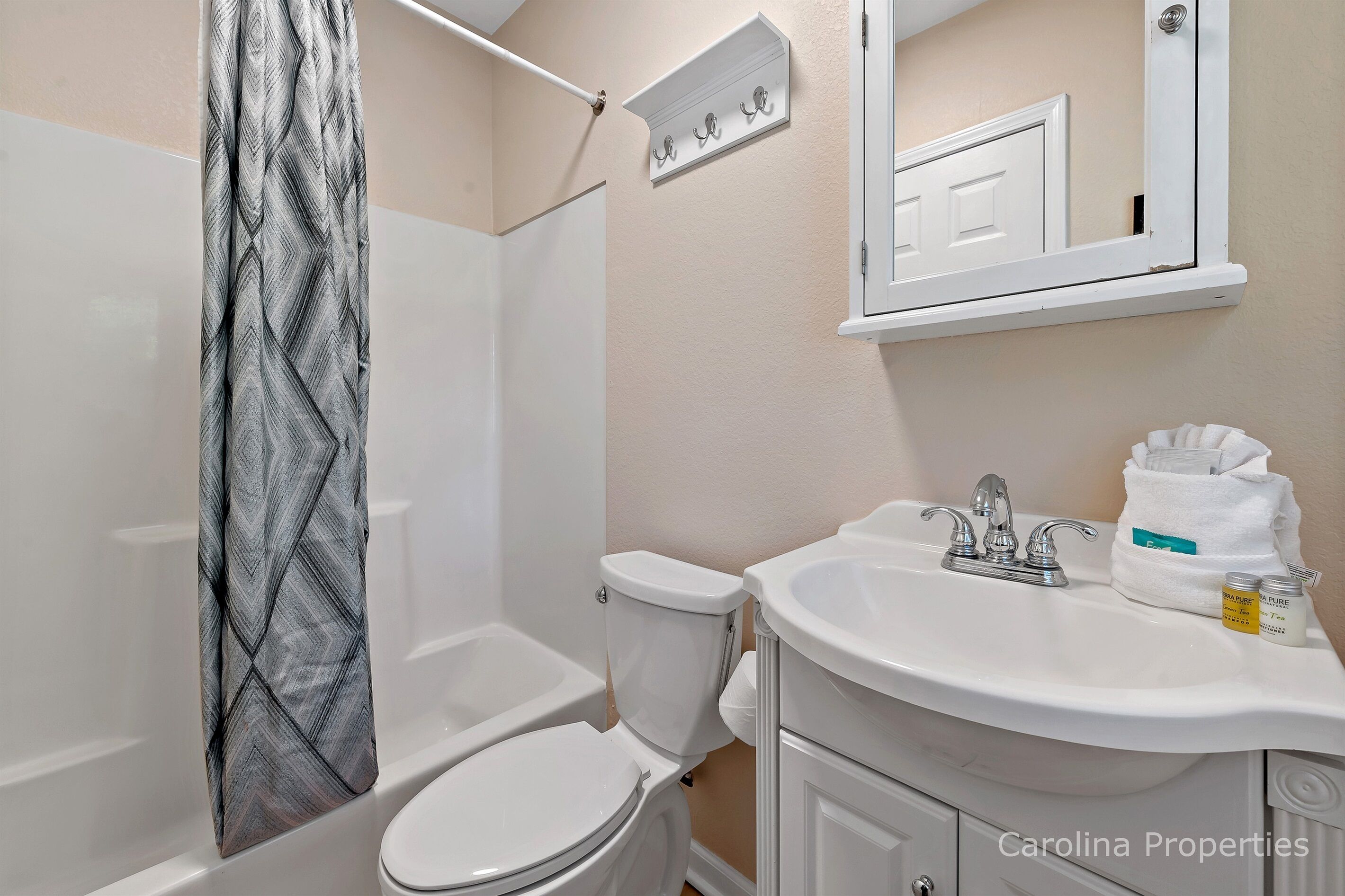 Une salle de bain avec un rideau de douche, des toilettes, un lavabo et un miroir au-dessus du lavabo.