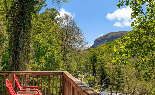 A wooden deck with red chairs overlooking a forested valley and a mountain.