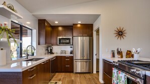 A modern kitchen with stainless steel appliances, wooden cabinets, and a tiled backsplash. - New Roadrunner heights (Joshua Tree)