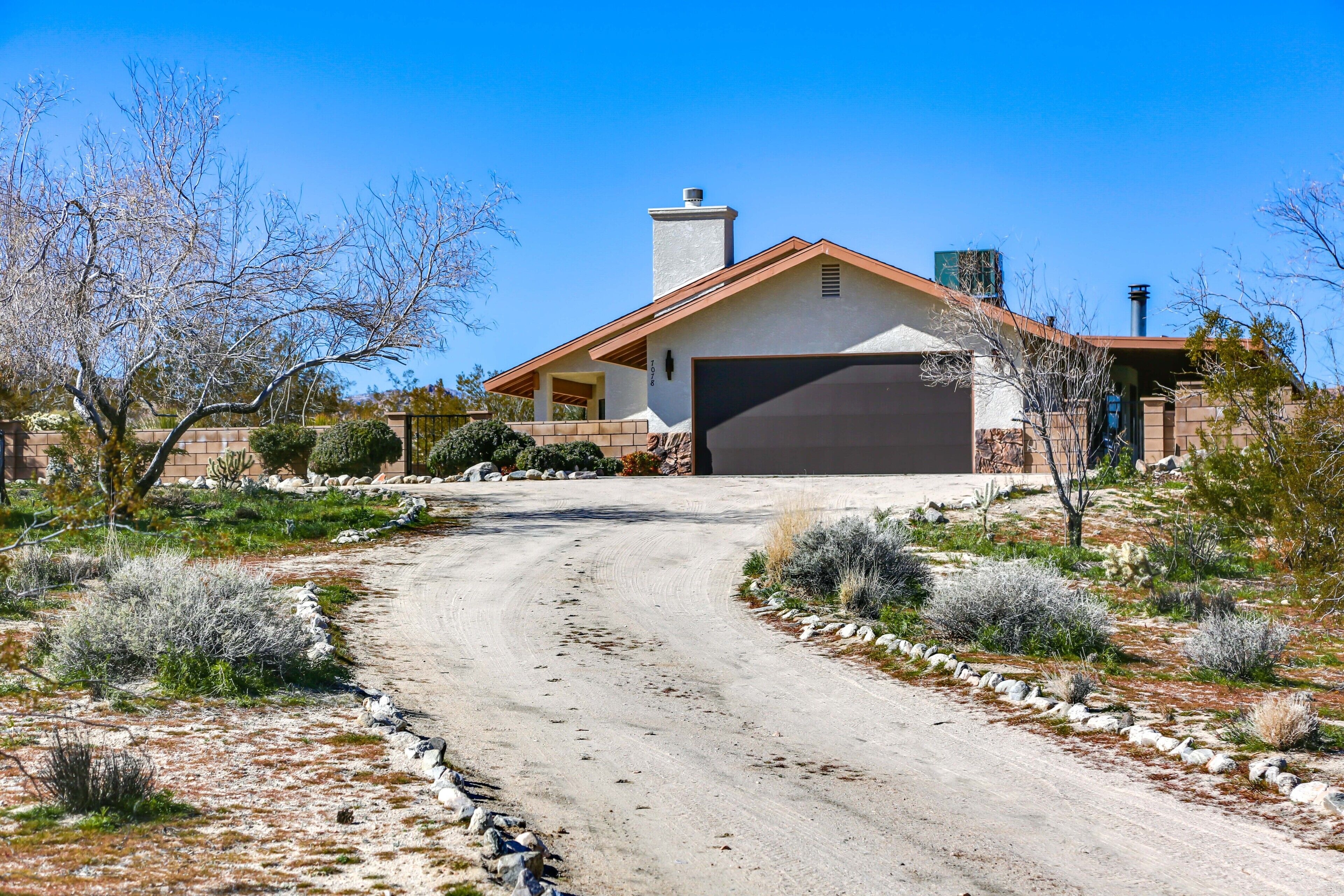 A house with a garage, surrounded by a desert landscape with sparse vegetation and a dirt road leading to the entrance.