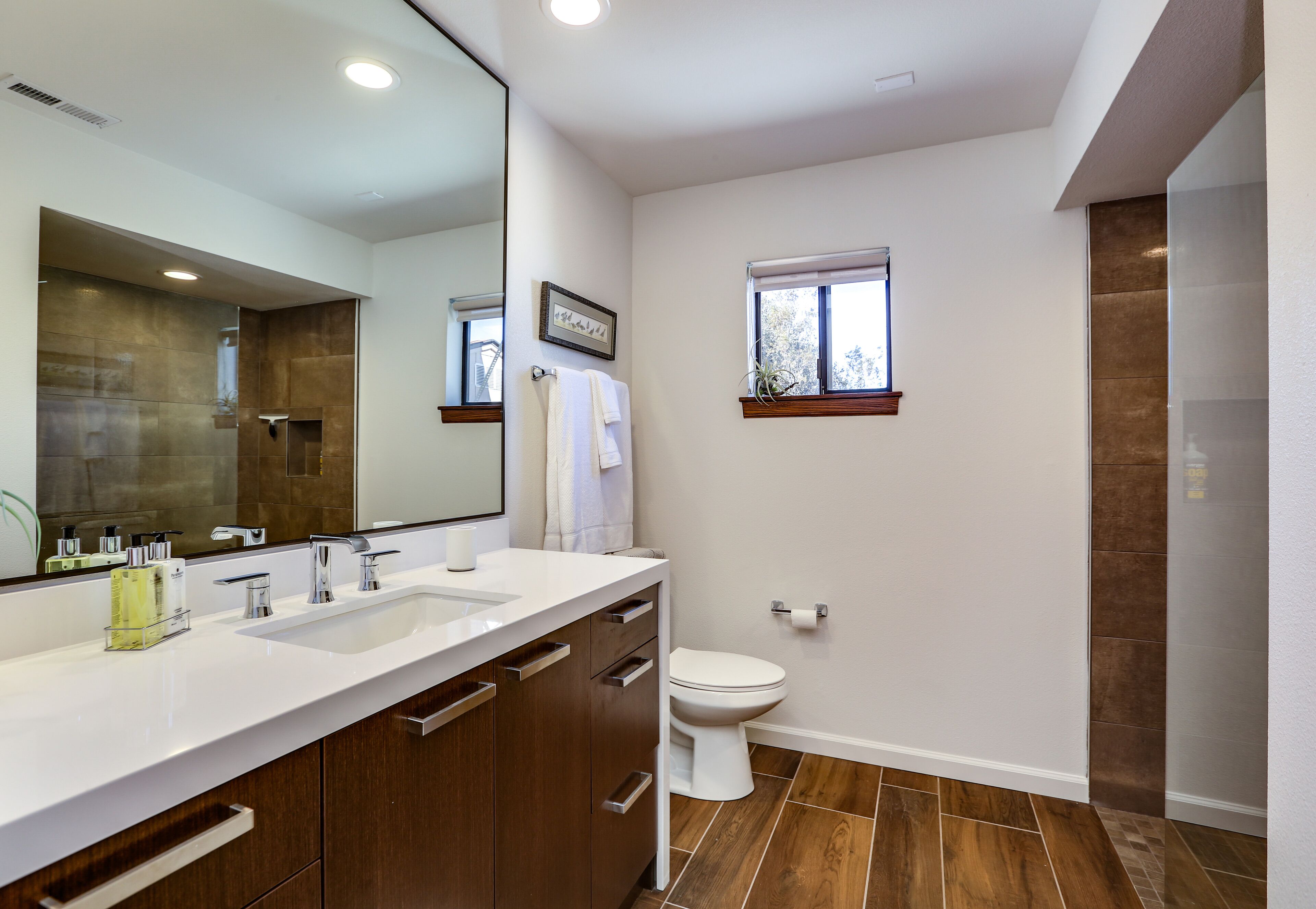 A modern bathroom with a large mirror, two sinks, a toilet, and a shower area.