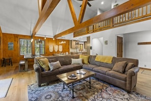 A spacious living room with a large sectional sofa, a coffee table, and a dining area with a kitchen in the background. - Total Privacy, Plus fun: Hot tub, pool table (Rockbridge)