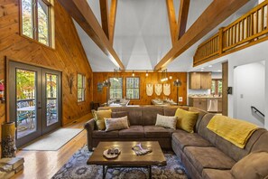 A spacious living room with a large sectional sofa, a coffee table, and a dining area with a table set for four. - Total Privacy, Plus fun: Hot tub, pool table (Rockbridge)