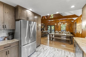 A modern kitchen with wooden cabinets, a stainless steel refrigerator, and a dining area with a long table and chairs. - Total Privacy, Plus fun: Hot tub, pool table (Rockbridge)
