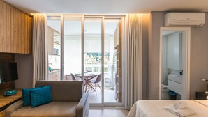Habitación de hotel con sofá, cama, televisor, baño y puerta corrediza de vidrio que da a un área exterior.