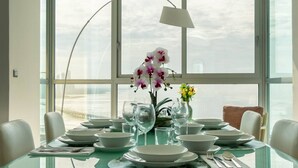 Mesa de comedor preparada para seis personas, con platos, tazones y vasos, un jarrón de orquídeas y una lámpara.