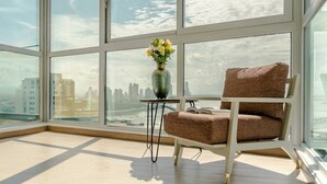 Una habitación moderna con un ventanal grande, un sillón tapizado en marrón, una mesita y un florero con flores.