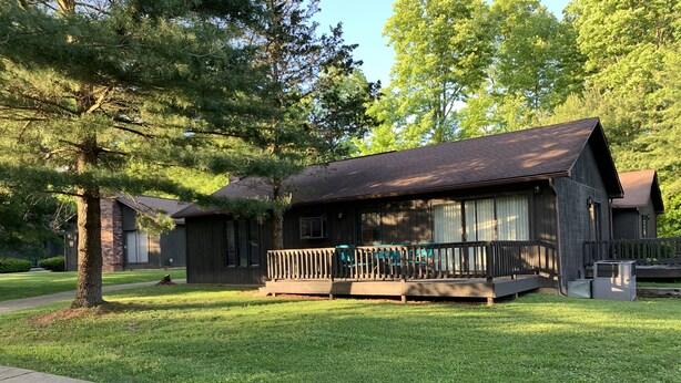 A lodge with a wooden exterior, a porch with chairs, and a well-maintained lawn. - The Pines of Apple Valley.  31 beautiful vacation cabins. (Howard)