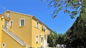Un edificio giallo con una scala che conduce a un balcone, immerso nel verde e sotto un cielo azzurro intenso.