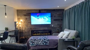 Ein modernes Wohnzimmer mit einem großen Flachbildfernseher, einem Kamin, Ledersitzmöbeln und einer gemütlichen Atmosphäre.
