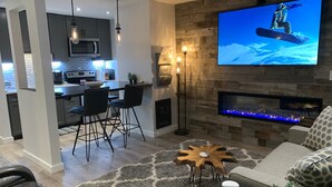 Ein modernes Wohnzimmer mit Flachbildfernseher, Kamin und einer Küche im Hintergrund.
