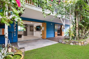 Una casa con fachada azul, un porche delantero y un jardín con diversas plantas y un pequeño estanque.