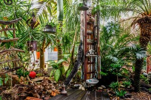 A rustic wooden structure with a sink, surrounded by lush tropical plants and a wooden deck. - Sandy Toes and Salty Kisses - Sunshine Coast (Marcoola)