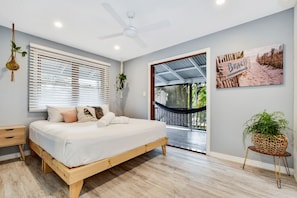 Un dormitorio con cama, ventilador de techo, ventana con persianas, una hamaca y decoración mural con temática playera.