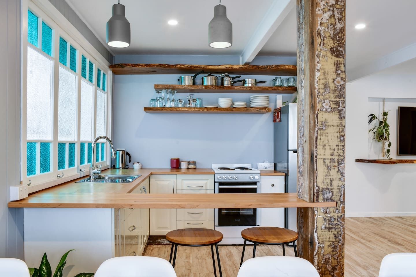 A modern kitchen with a central island, wooden shelves, and a large window with blue-tinted glass.