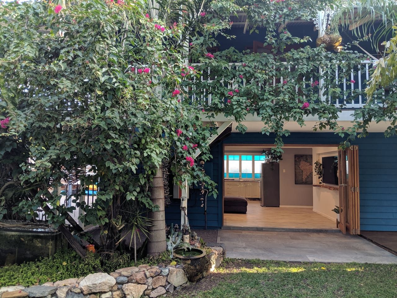 A house with a covered patio, a stone wall, and a garden with flowering plants.