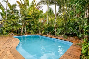 Una piscina con bordo in legno, circondata da una rigogliosa vegetazione tropicale.