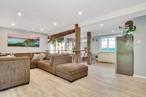 A spacious living area with a sectional sofa, a dining table, and a kitchen area with a refrigerator. - Sandy Toes and Salty Kisses - Sunshine Coast (Marcoola)