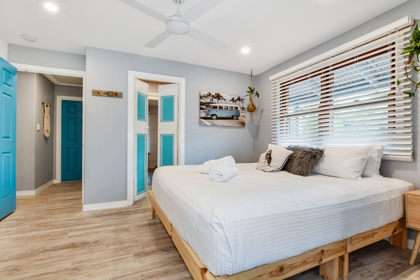 A bedroom with a bed, a ceiling fan, a window with blinds, and a door leading to another room.
