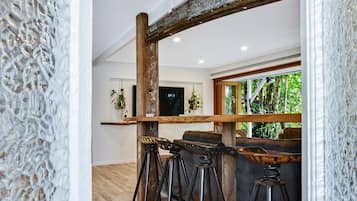 A modern interior with a wooden bar, stools, and a view of greenery outside.