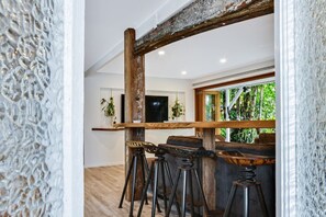 Un interno moderno con un bancone in legno, sgabelli e vista su spazi verdi esterni.