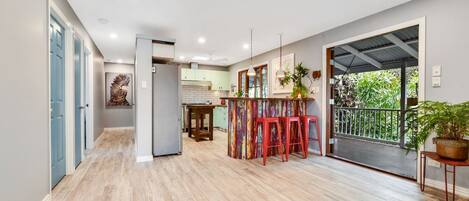 A spacious kitchen with a dining area, wooden flooring, and a view through a sliding door to an outdoor balcony.