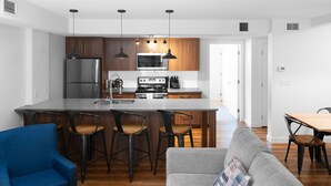 A modern kitchen with a central island, bar stools, a dining table, a sofa, and a blue armchair. - Basecamp Resorts Canmore I One Bedroom Apartment, Dog Friendly (Canmore)
