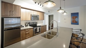 A modern kitchen with stainless steel appliances, wooden cabinets, and a large island with a sink. - Basecamp Resorts Canmore I One Bedroom Apartment, Dog Friendly (Canmore)