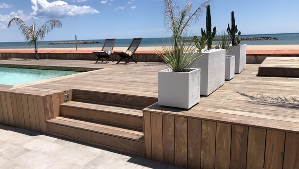 Een houten terras met een zwembad, ligbedden en potplanten.