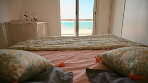 Een slaapkamer met een bed, een dressoir en uitzicht op het strand.